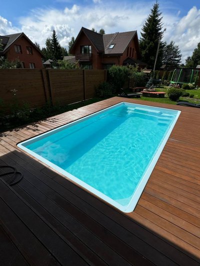 Прямоугольный бассейн с террасой из темного дерева и зеленым газоном вокруг